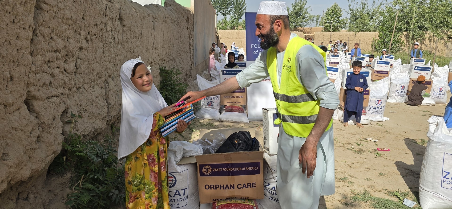 A smiling Afghan orphan girl receives notebooks thanks to your support through Zakat Foundation of America, empowering her education and future.