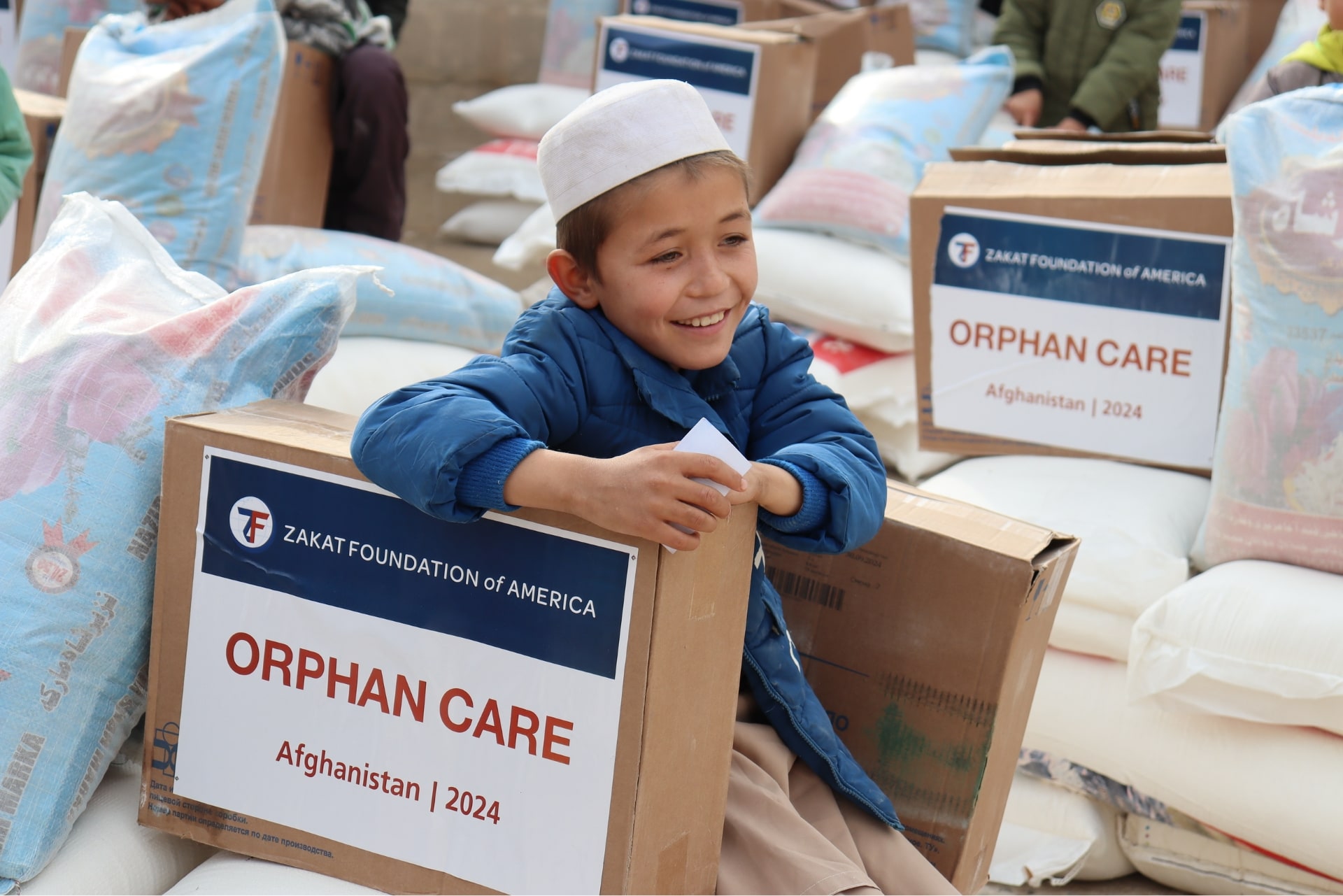 An orphaned Afghan boy sits with an expression of relief on his face after receiving essential supplies from supporters like you.