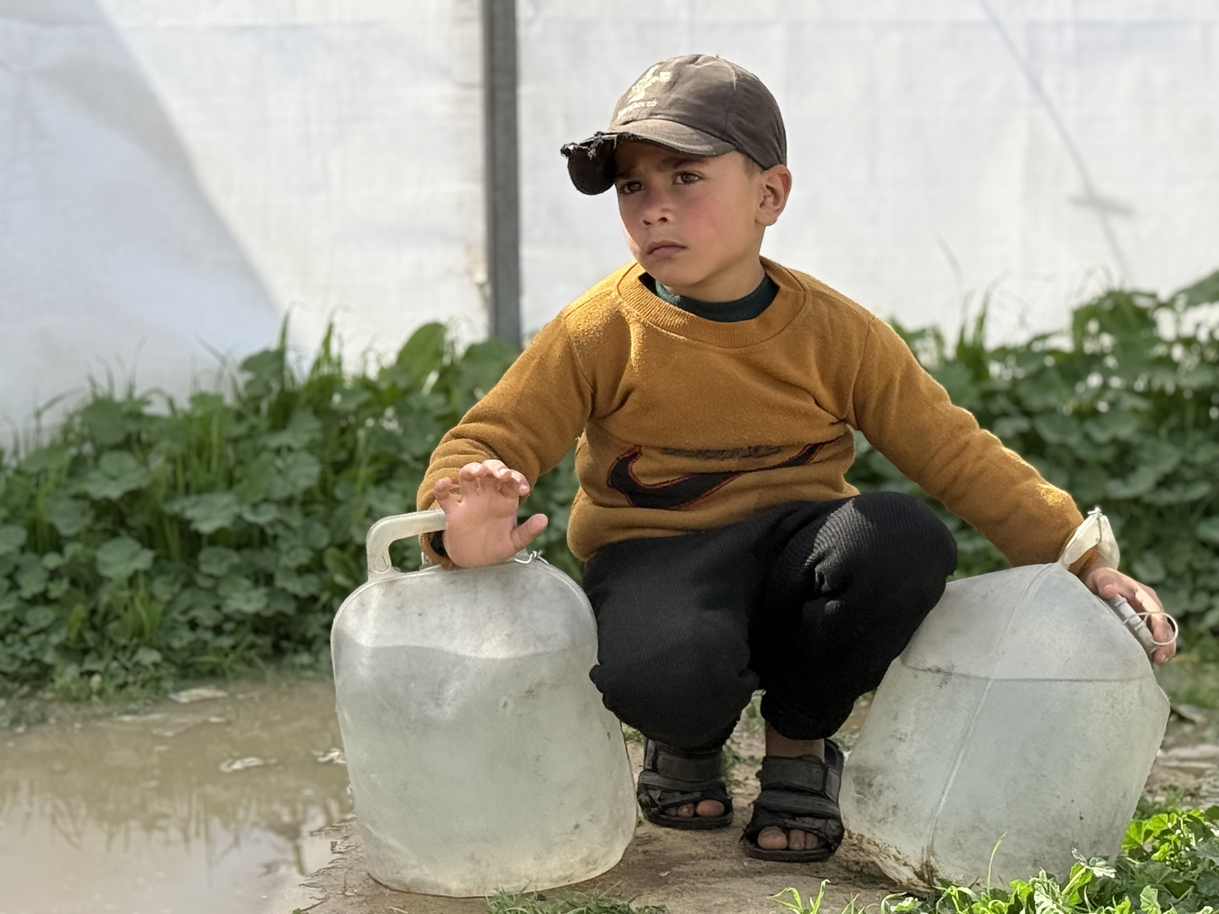 A boy in Gaza rests after carrying jugs of clean water from our distribution site