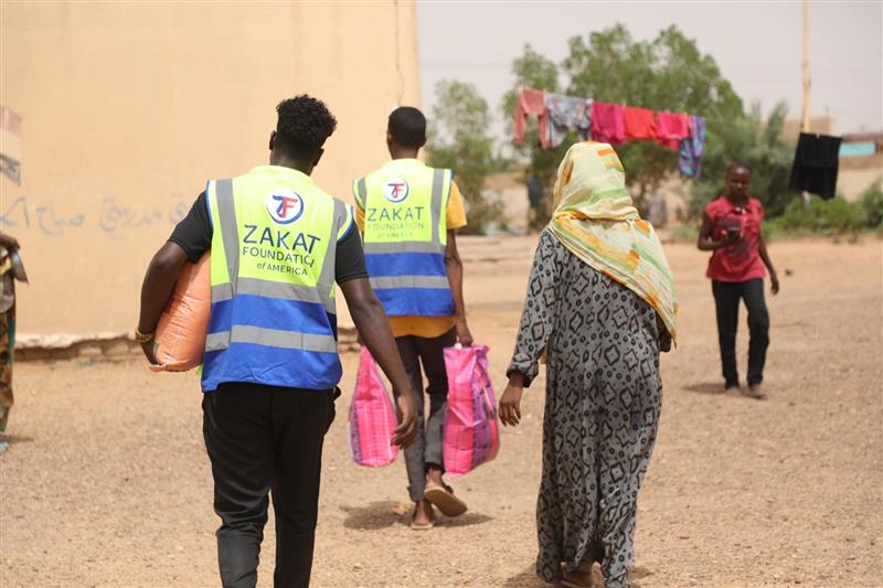 Our teams help carry supplies for an older woman displaced in Sudan