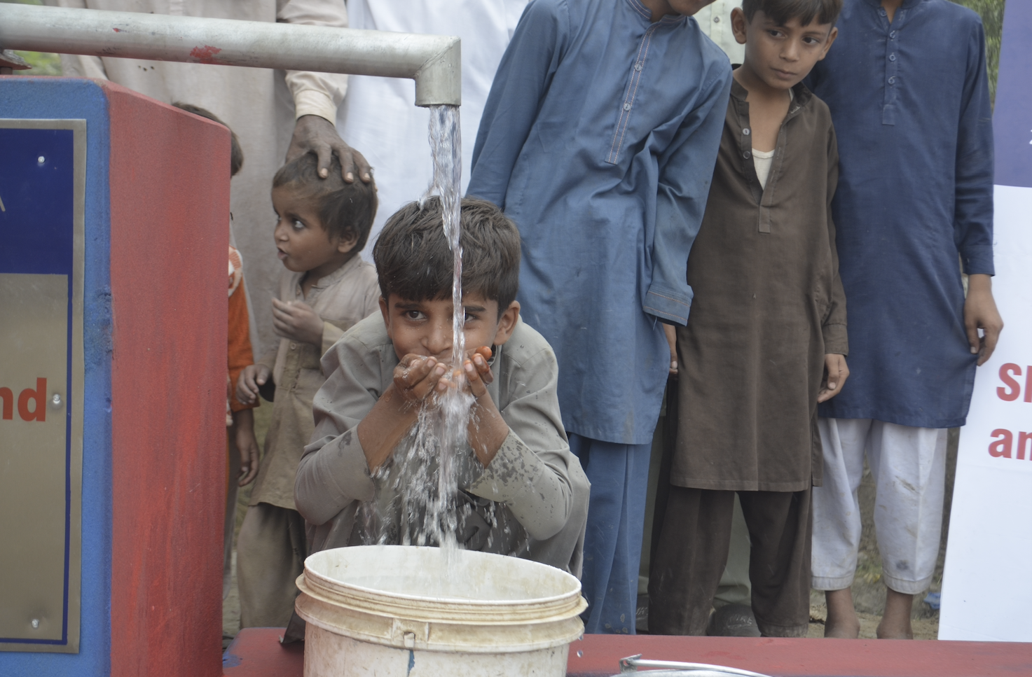 A young boy in Pakistan takes a sip of water from our pump during collection